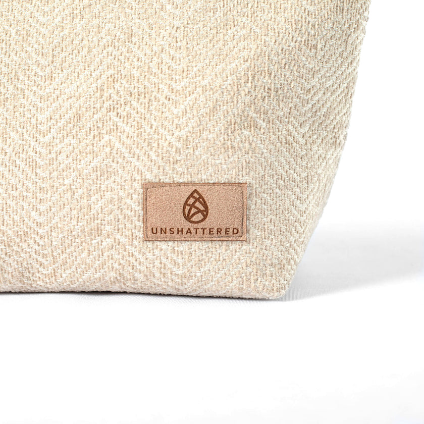 Tan suede Unshattered label on a beige textured upcycled fabric makeup bag on a white background