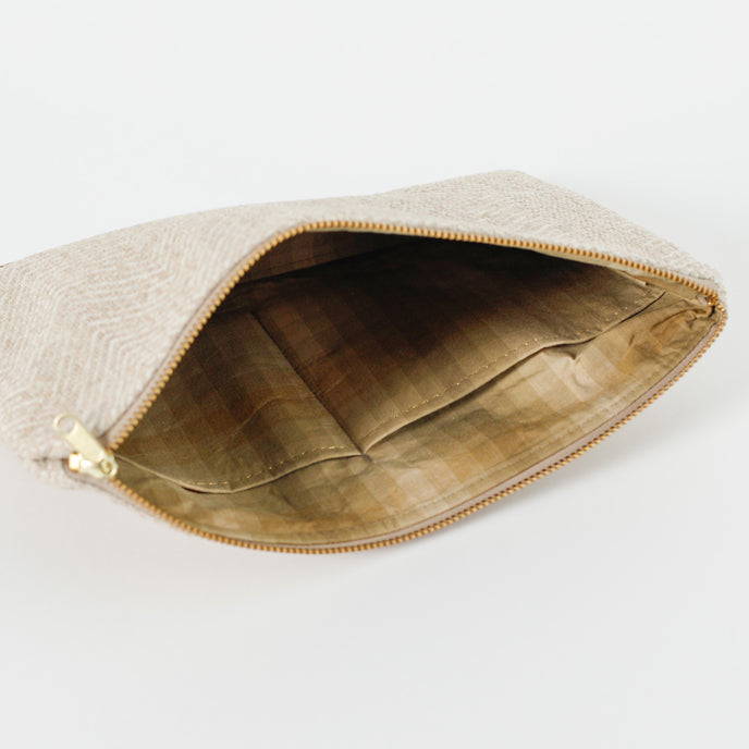A different colored tans and brown  checkered fabric interior with gold tone hardware on a beige large zip pouch 