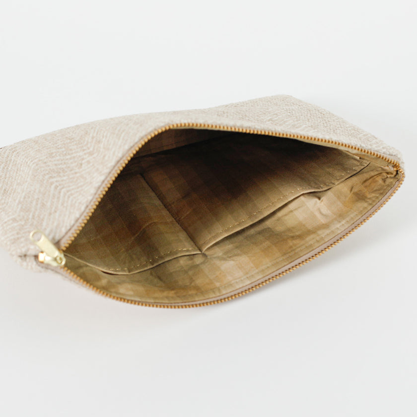 A different colored tans and brown  checkered fabric interior with gold tone hardware on a beige large zip pouch 