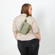 Woman wearing an olive green vegan leather crossbody bag on her back with a white background named after Tasha