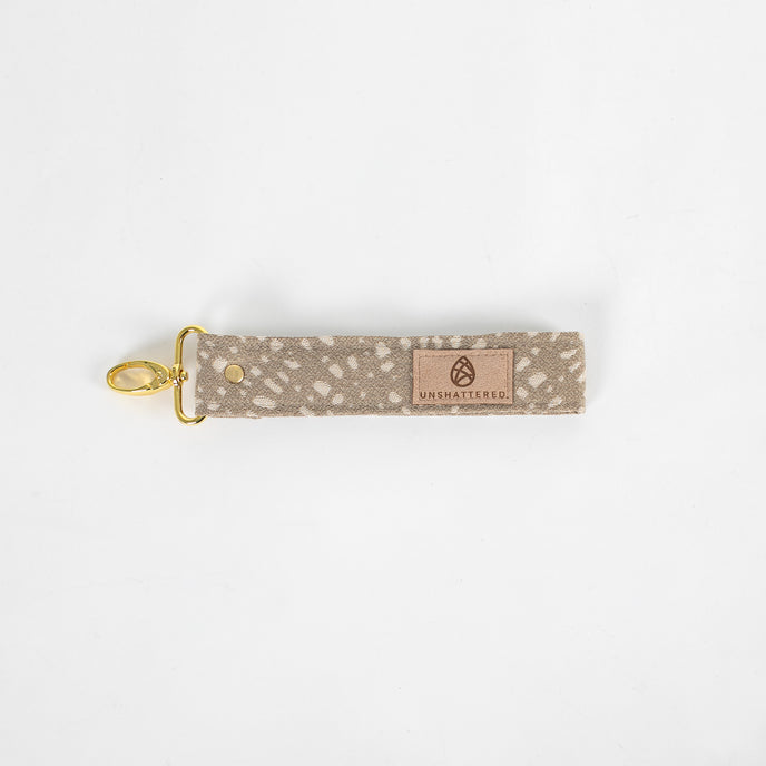 This beige fabric wristlet key clip features a playful dotted pattern and sleek gold-tone hardware.