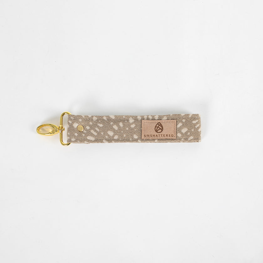 This beige fabric wristlet key clip features a playful dotted pattern and sleek gold-tone hardware.