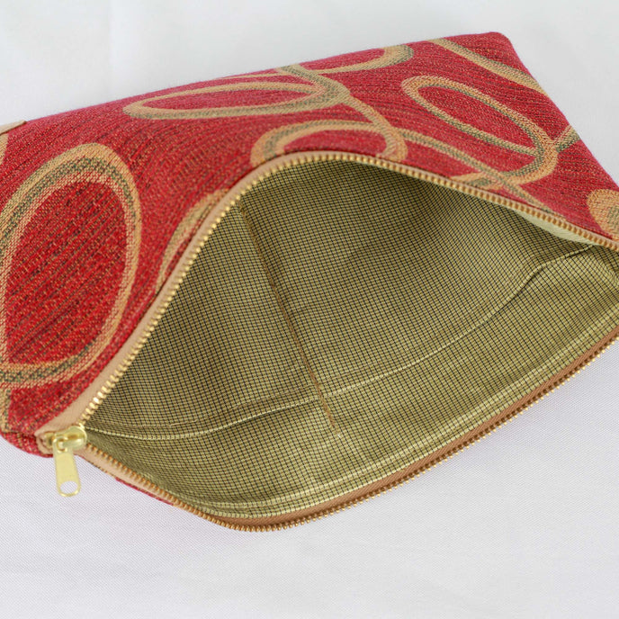 A green and blue checkered fabric interior with a gold tone zipper on a red large zip pouch with gold and green swirls on the outside 