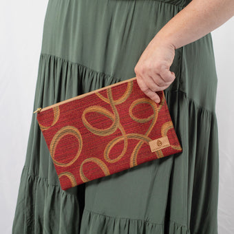 A woman wearing a green dress holding a red large zip pouch with geometric pattern with a tan label 
