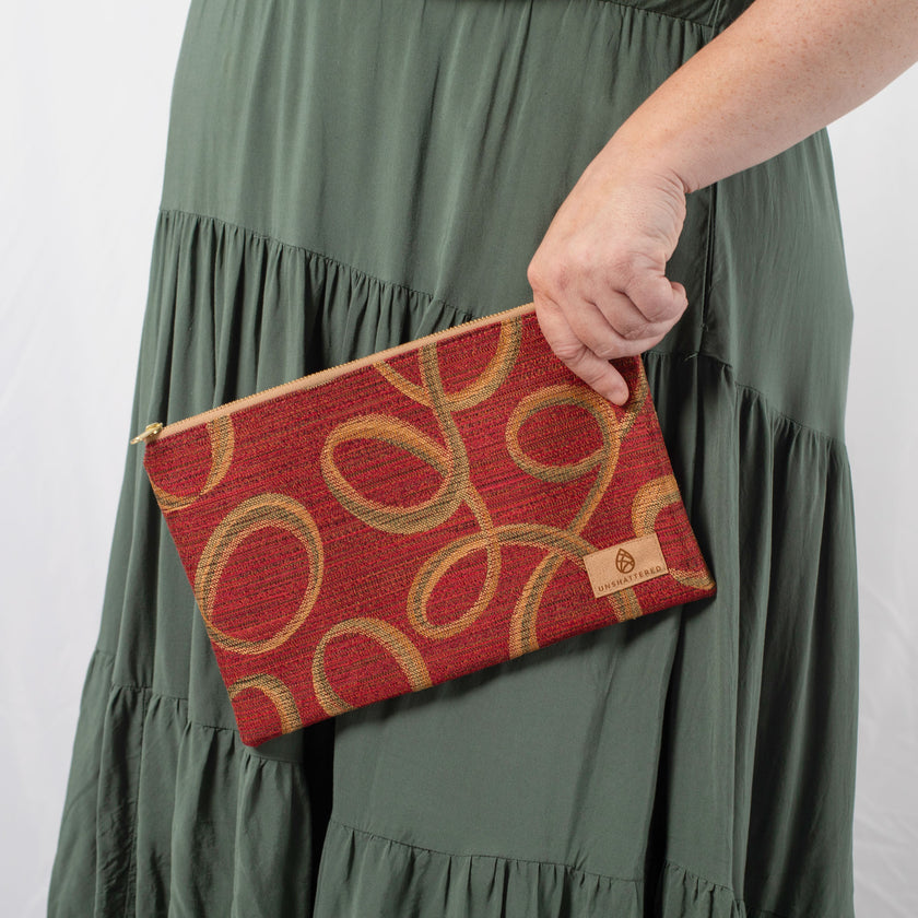 A woman wearing a green dress holding a red large zip pouch with geometric pattern with a tan label 