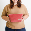 A woman holding a red makeup bag with a tan Unshattered label named after Tirza