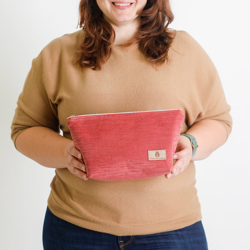 A woman holding a red makeup bag with a tan Unshattered label named after Tirza