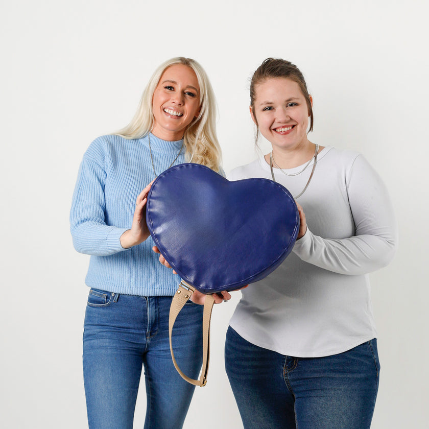 Two people holding a blue heart bag made from upcycled Southwest Airlines seat leather against a white background