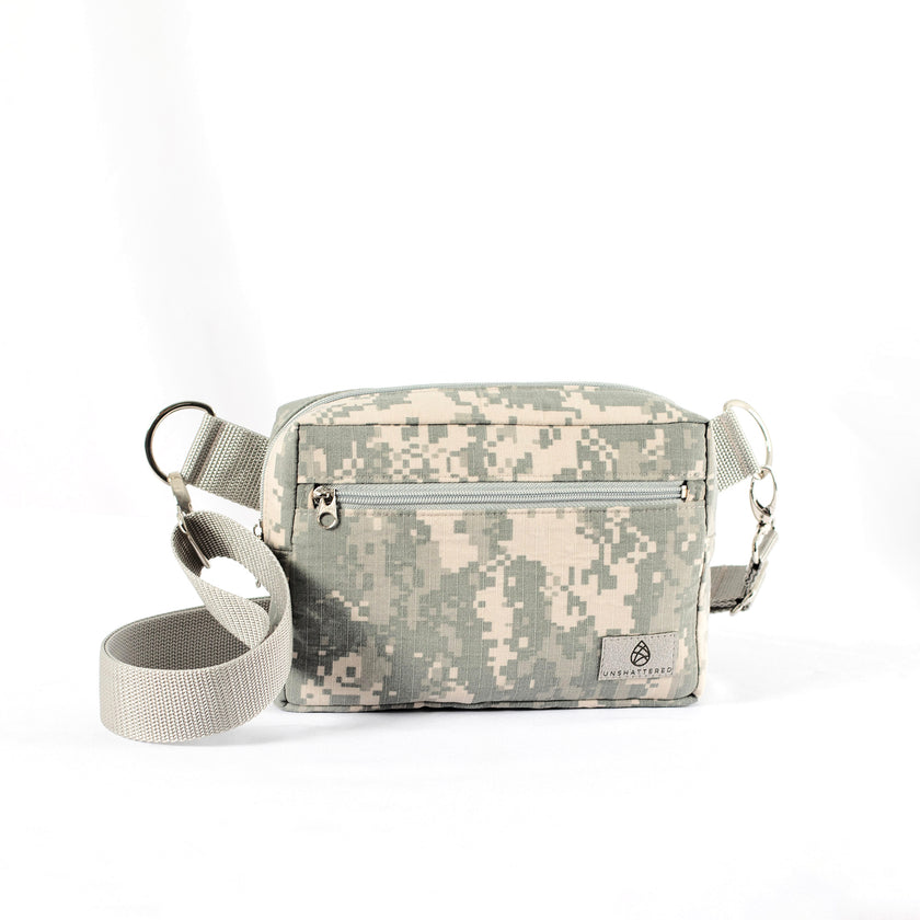 An errand bag handcrafted from upcycled digital camo army uniform with an adjustable strap and a front zippered pocket on a white background.