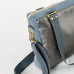 A gray strap with gold hardware on a charcoal luxury leather alternative with blue velvet accents 