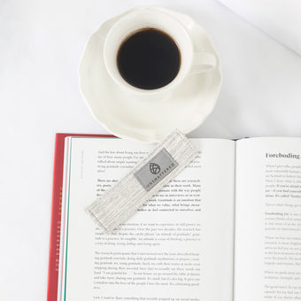 White mug with black coffee on an open book silver bookmark