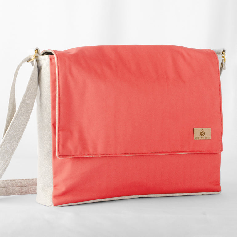 A red and white large messenger bag made from formula e racing material with an adjustable strap, shown with a focus on the front pocket and the brand's tag 
