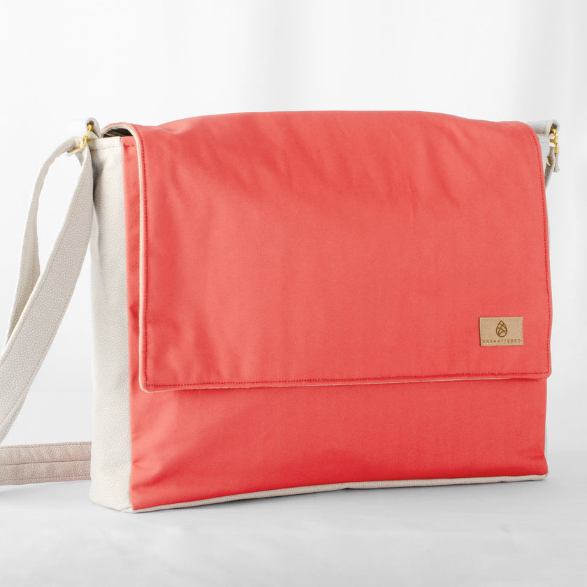 A red and white large messenger bag made from formula e racing material with an adjustable strap, shown with a focus on the front pocket and the brand's tag 