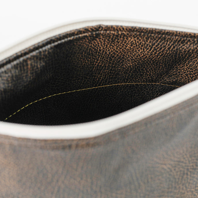 A brown luxury leather alternative interior with a gold seam on the inside of a makeup bag