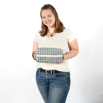 A woman holding a blue and white plaid toiletry with a gray label 