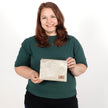 Woman holding a beige zip pouch handcrafted from upcycled fabric with a delicate ivy pattern against a plain background named after Kathleen 