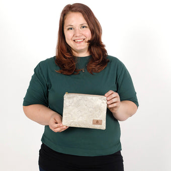 Woman holding a beige zip pouch handcrafted from upcycled fabric with a delicate ivy pattern against a plain background named after Kathleen 