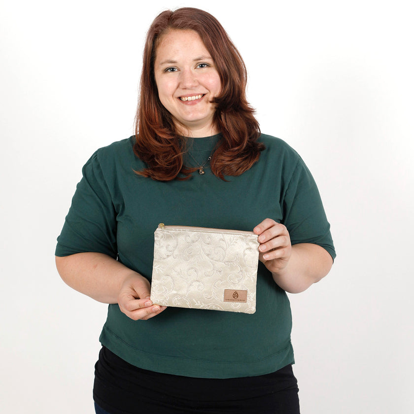 Woman holding a beige zip pouch handcrafted from upcycled fabric with a delicate ivy pattern against a plain background named after Kathleen 