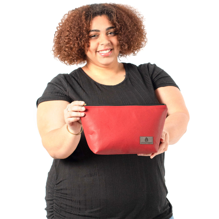 A woman holding a red luxury leather alternative makeup bag with a gray Unshattered label and a black zipper with gold-tone hardware