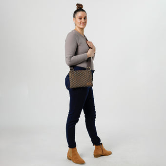 Woman holding a brown and blue geometric print fabric crossbody pouch on a white background
