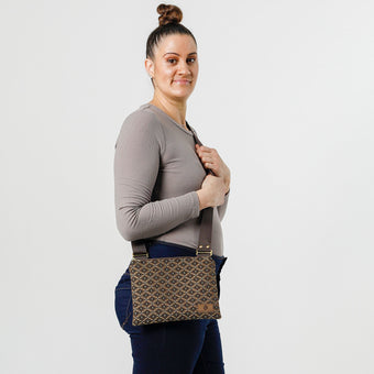 A woman carrying a  brown and blue geometric print fabric crossbody pouch with a zipper closure and an adjustable brown strap, named after Amy. 