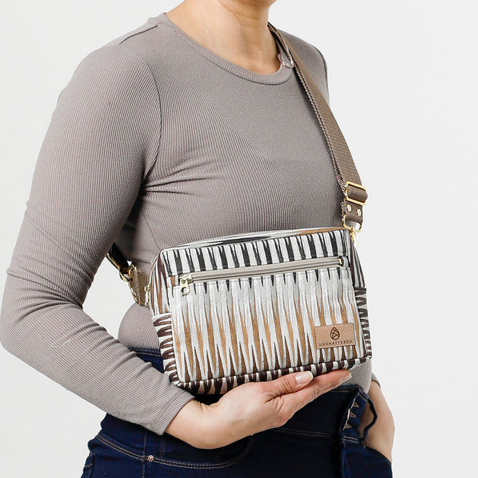 A woman wearing a handcrafted errand bag with a brown chevron pattern in muted colors with a front zip pocket and an adjustable strap named after Sally