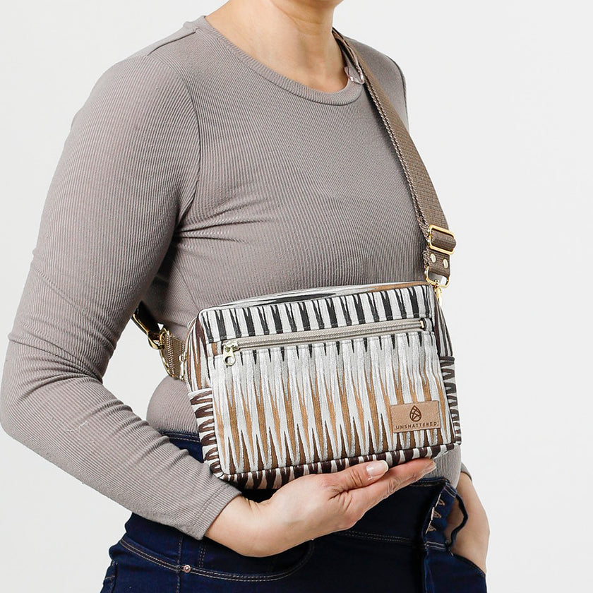 A woman wearing a handcrafted errand bag with a brown chevron pattern in muted colors with a front zip pocket and an adjustable strap named after Sally