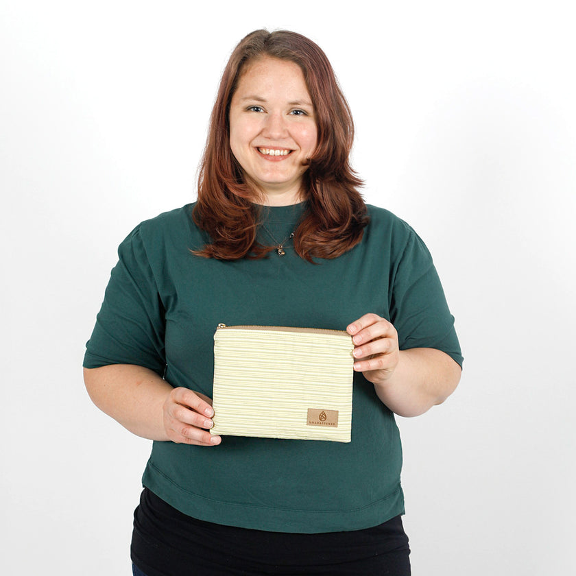 Woman holding a  light yellow striped zip pouch named Katya and made from upcycled materials on a white background