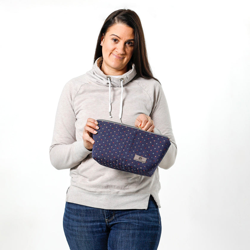 Woman holding a navy blue makeup pouch made from upcycled materials and named in honor of Brianne against a white background