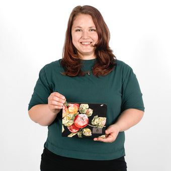 Woman holding a floral and fruit design pouch made from upcycled material against a white background