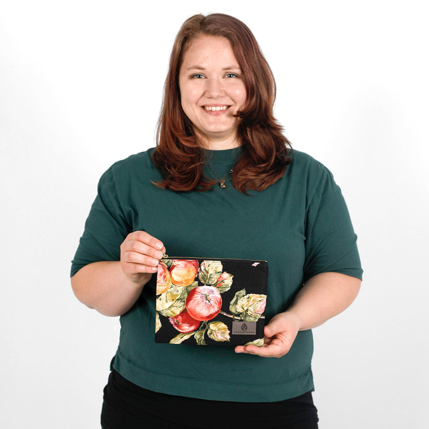 Woman holding a floral and fruit design pouch made from upcycled material against a white background
