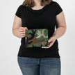 A woman holding a woodland camo zippered pouch with a brown label 