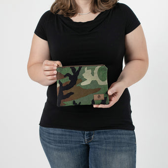 A woman holding a woodland camo zippered pouch with a brown label 