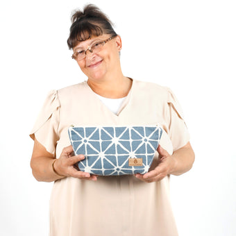 Woman holding the Erin Makeup Bag handcrafted from upcycled blue geometric patterned fabric on a white background