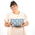 Woman holding the Erin Makeup Bag handcrafted from upcycled blue geometric patterned fabric on a white background