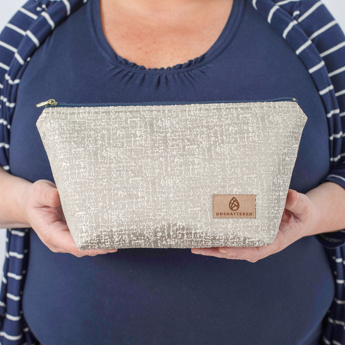 A woman holding a neutral style makeup kit with a tan label and a gold tone zipper