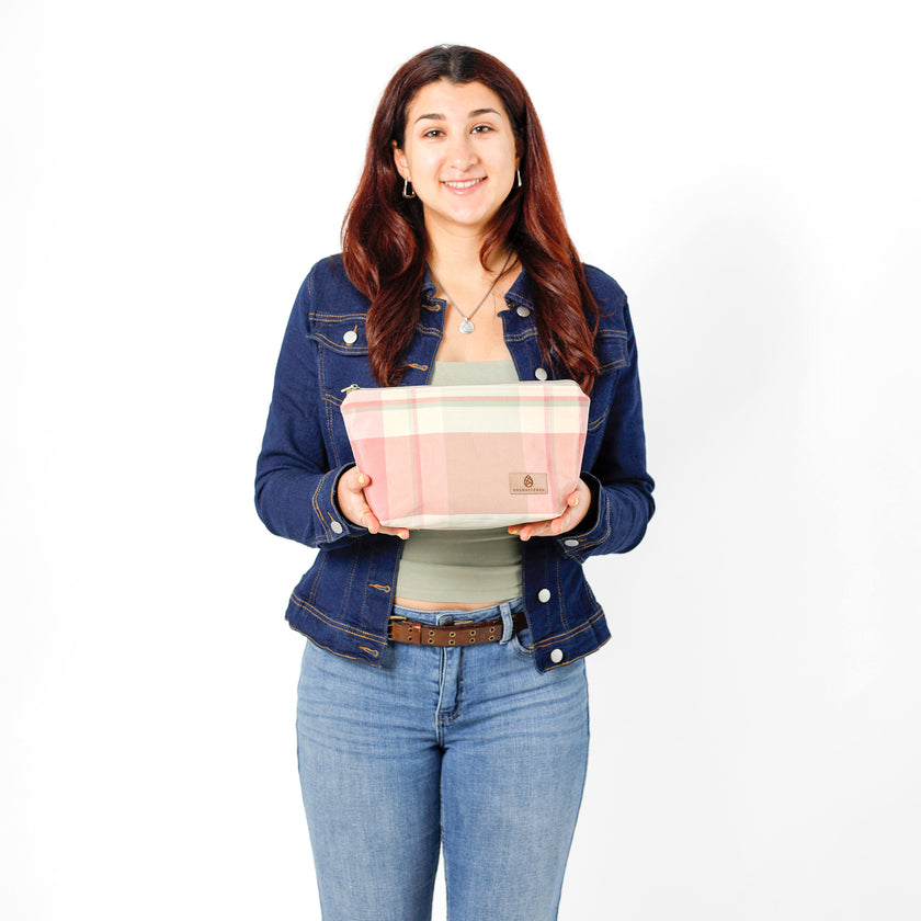 Woman holding a makeup bag named Quela handcrafted from upcycled pastel plaid fabric in hues of pink and green.