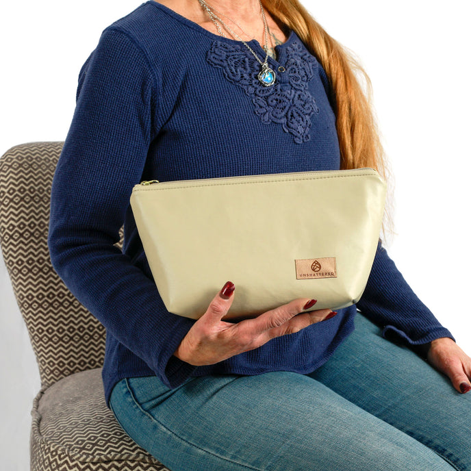 Woman holding a beige wipe-clean makeup bag, sitting on a patterned chair.