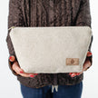 Woman holding a makeup bag named Theresa handcrafted from upcycled textured beige material