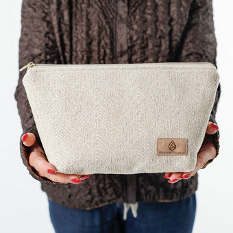 Woman holding a makeup bag named Theresa handcrafted from upcycled textured beige material