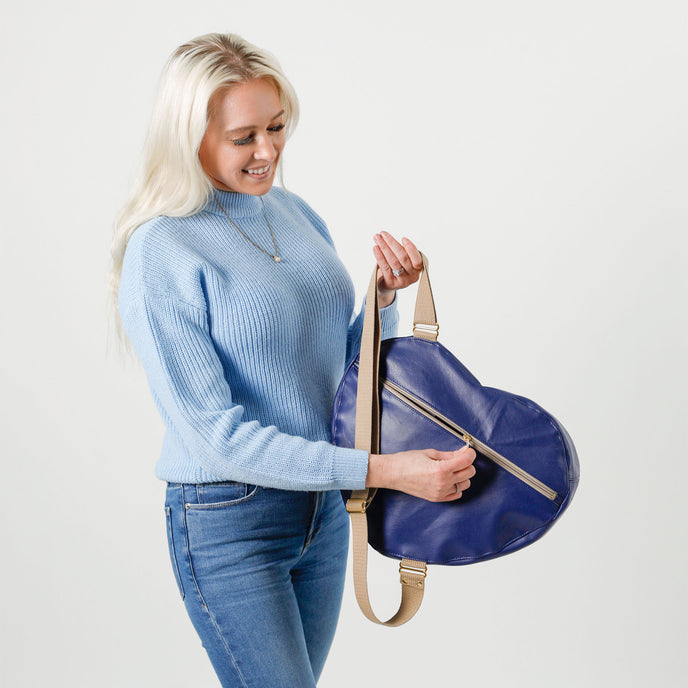 Woman opening a tan zippered pocket on the back of a blue heart bag made from upcycled southwest airlines seat leather 