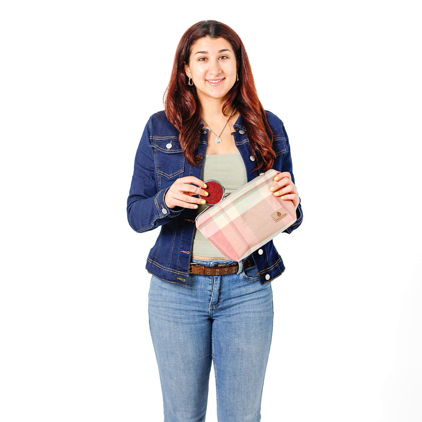 Woman putting a compact mirror into a makeup bag named Quela handcrafted from upcycled pastel plaid fabric in hues of pink and green.