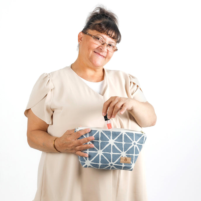 Woman putting lip gloss into the Erin Makeup Bag handcrafted from upcycled blue geometric patterned fabric on a white background