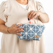Woman putting lip gloss into the Erin Makeup Bag handcrafted from upcycled blue geometric patterned fabric on a white background