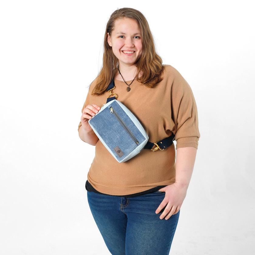 A woman wearing a blue errand bag across her chest with blue straps and gold hardware 