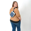 A woman wearing a blue velvet errand bag on her back smiling on a white background 