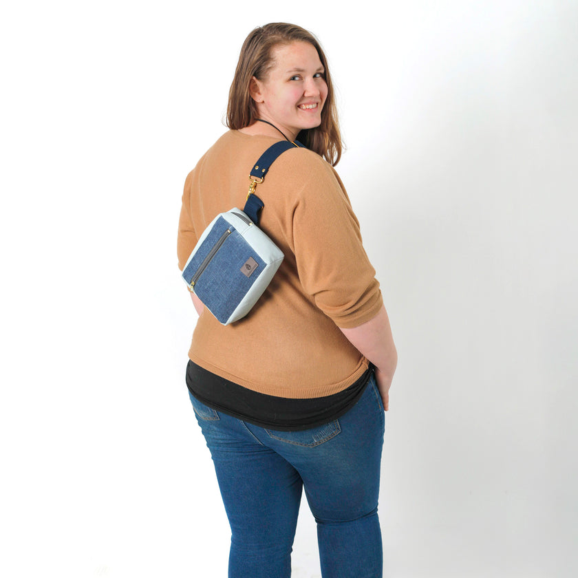 A woman wearing a blue velvet errand bag on her back smiling on a white background 