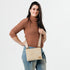 A woman carrying a beige crossbody pouch with a white circle pattern and tan strap and gold hardware 