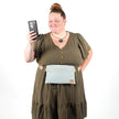 Woman looking at a phone while wearing a light blue 3-in-1 bag named George hands free belt bag style against a white background 