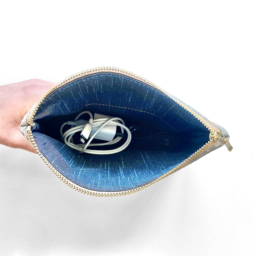 Zip pouch with blue fabric interior with gold zipper containing charging cords on a white background